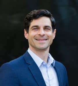 A Man Wearing A Suit And Tie Smiling At The Camera